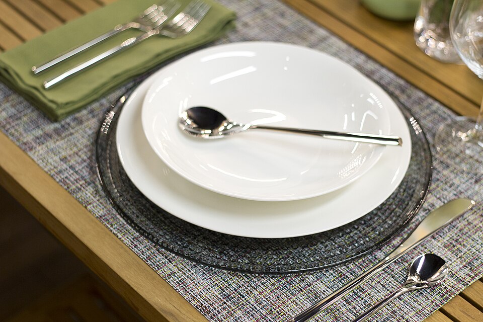 A dining place setting with a glass charger plate and cutlery