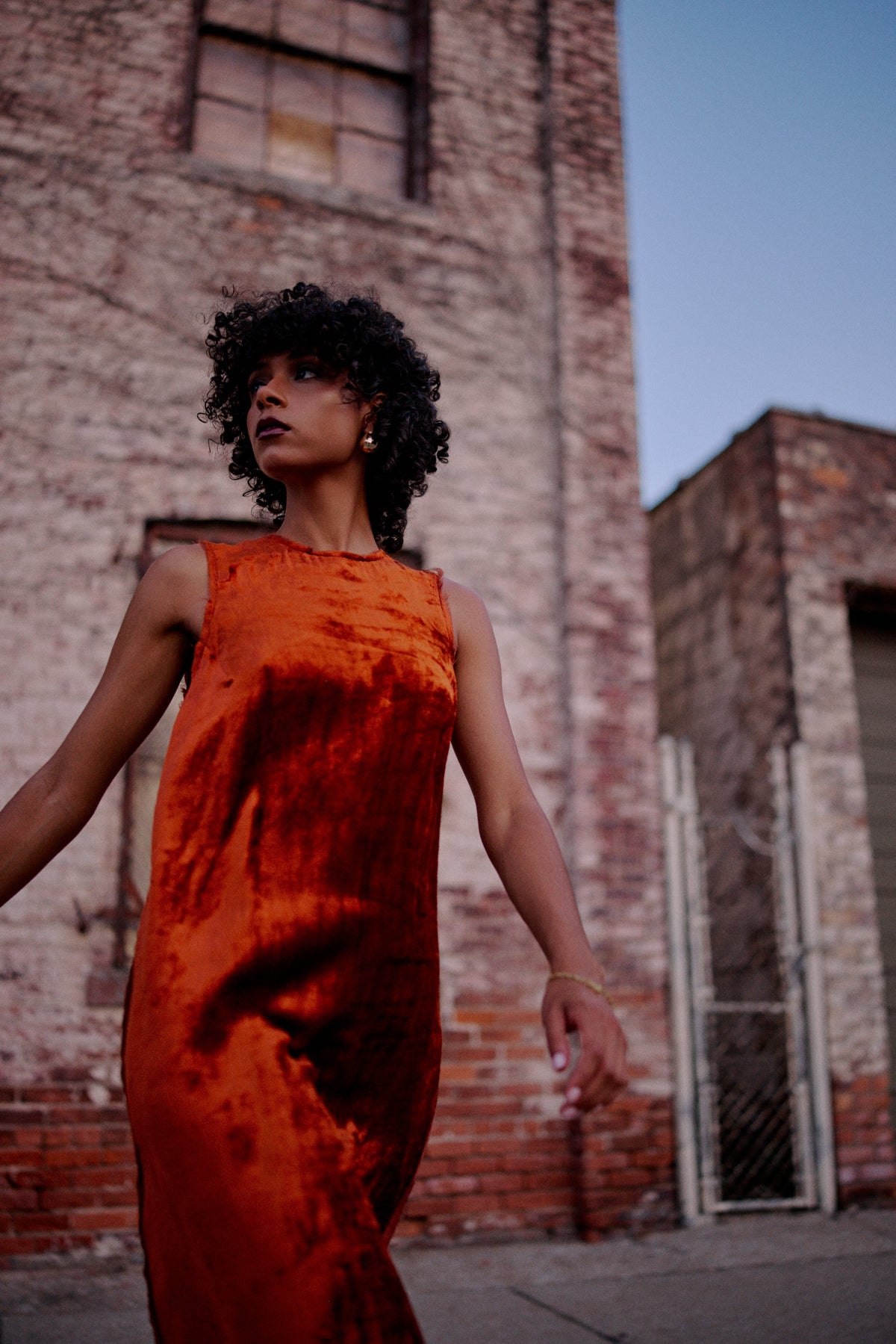 Model wearing a rust colored velvet dress against a brick wall