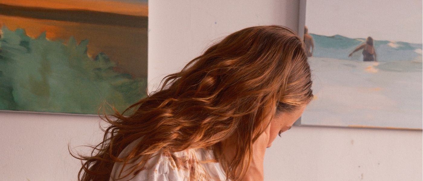 Kate Keery in front of paintings of a green landscape and a figure standing in pale water