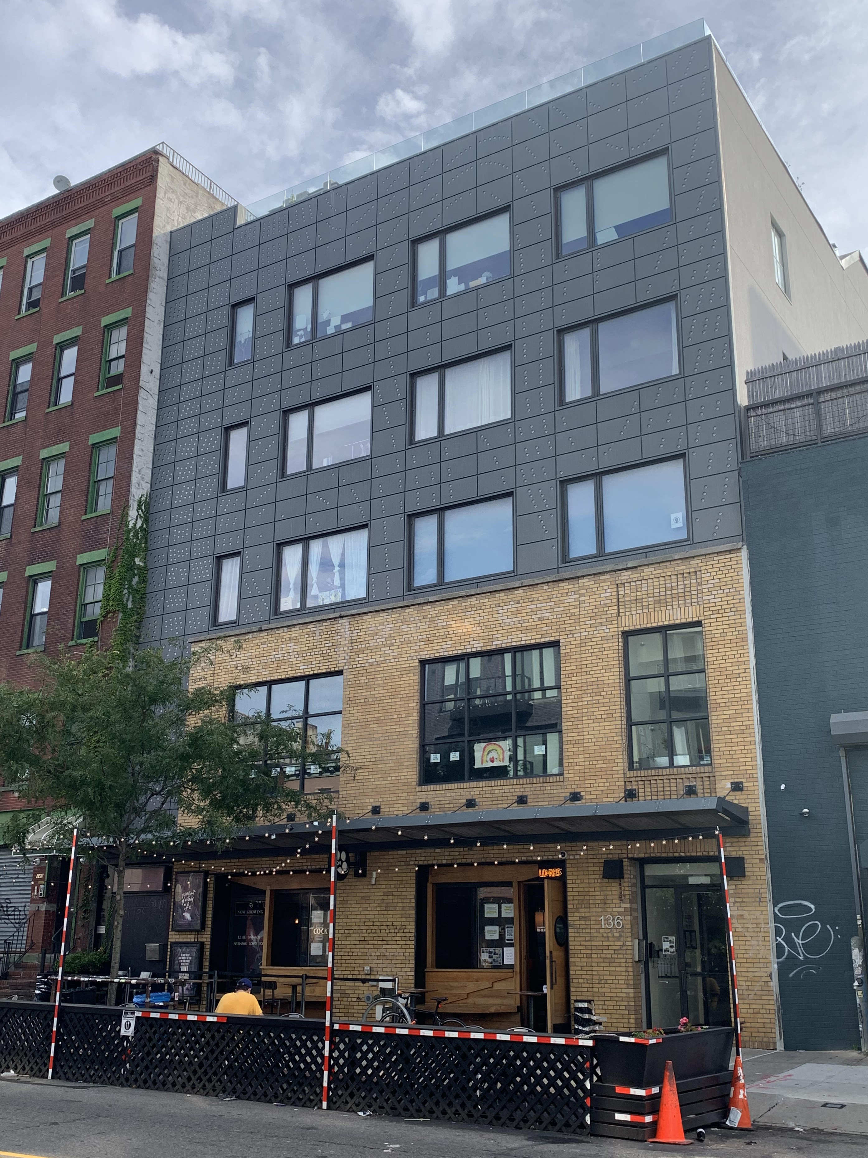 Nitehawk Cinema Williamsburg entrance at 136 Metropolitan Avenue with outdoor tables beneath a gray metal facade